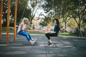 two women facing each other on swings and laughing together