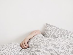 photo of a white wall and white comforter with a sleeping person's hand over top of the blanket