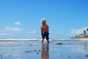 picture of a toddler boy wading into the ocean looking away from the camera