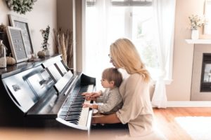 mom holding toddler son and playing piano together