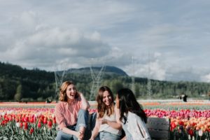 3 women laughing together on a bench in front of a field of colorful tulips