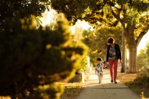 grandma and little girl holding hands walking on sidewalk at golden hour