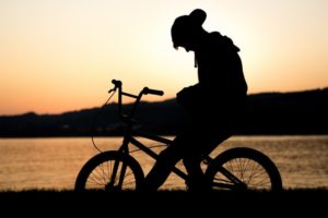 silhouette of a teenage boy at sunset on his bike looking down