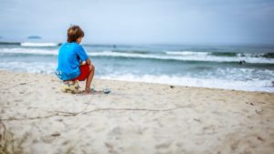 elementary school aged boy sitting on a soccer ball looking out into the ocean