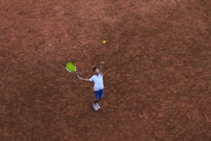 overhead picture of a boy throwing a tennis ball up in the air getting ready to hit it