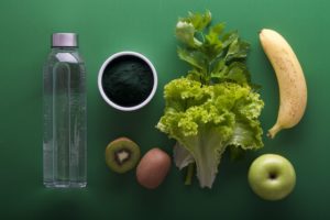 flat lay picture of a water bottle and a variety of fruits and vegetables on a green background