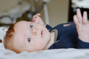 photo of a baby boy laying on his back looking wide eyed at camera