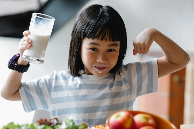 young girl drinking milk and flexing her arm muscle