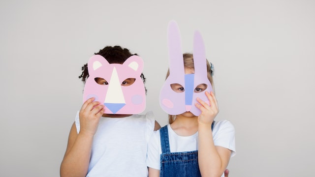 two kids holding up pink animal face masks