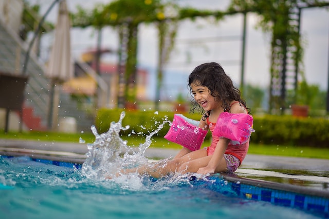 girl sitting on side of pool laughing, while kicking up water