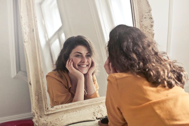 confident woman smiling into mirror at self