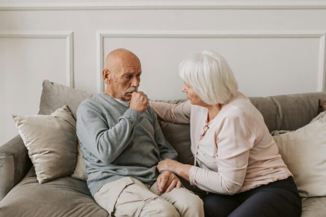 senior man coughing on couch with senior woman