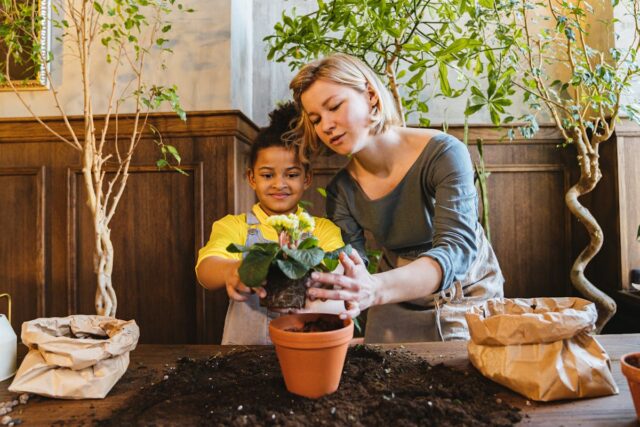 boy planting flower in pot with mom