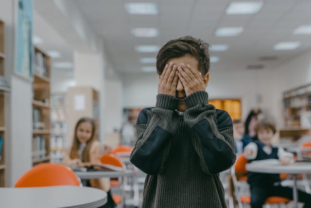 boy covering eyes in classroom
