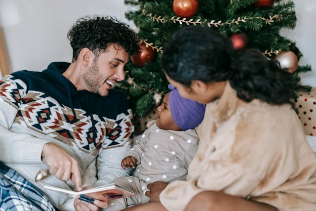 parents reading baby a book under the Christmas tree