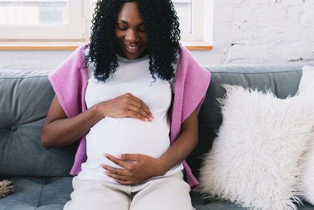 woman holding pregnant belly while sitting on couch