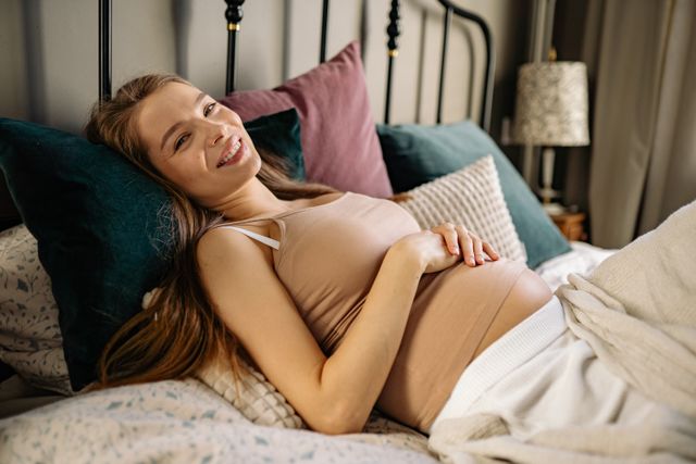 woman laughing holding pregnant belly on bed
